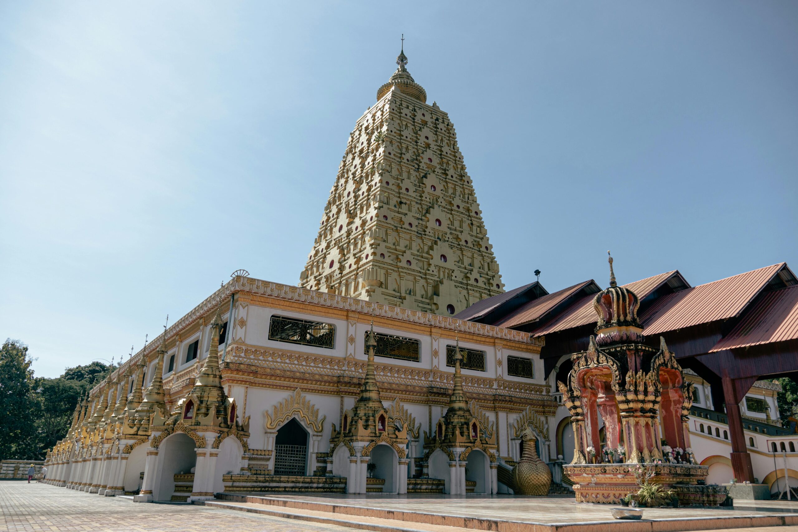 Ornate Buddhist temple with golden tower and intricate designs under a clear blue sky.